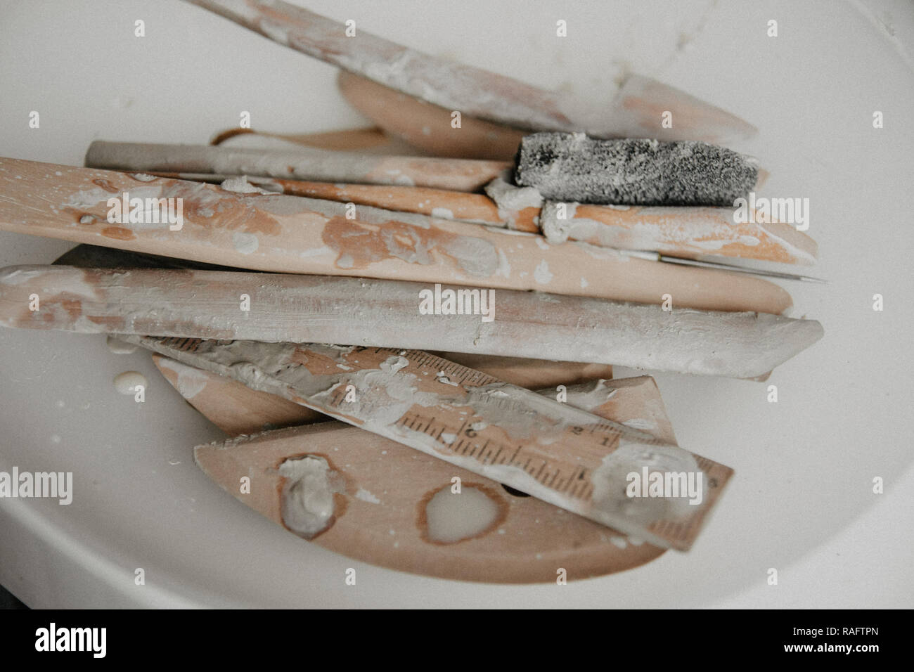 Set di sporco arte e artigianato scultura strumenti sul tavolo di legno nel laboratorio di ceramica su sfondo chiaro Foto Stock