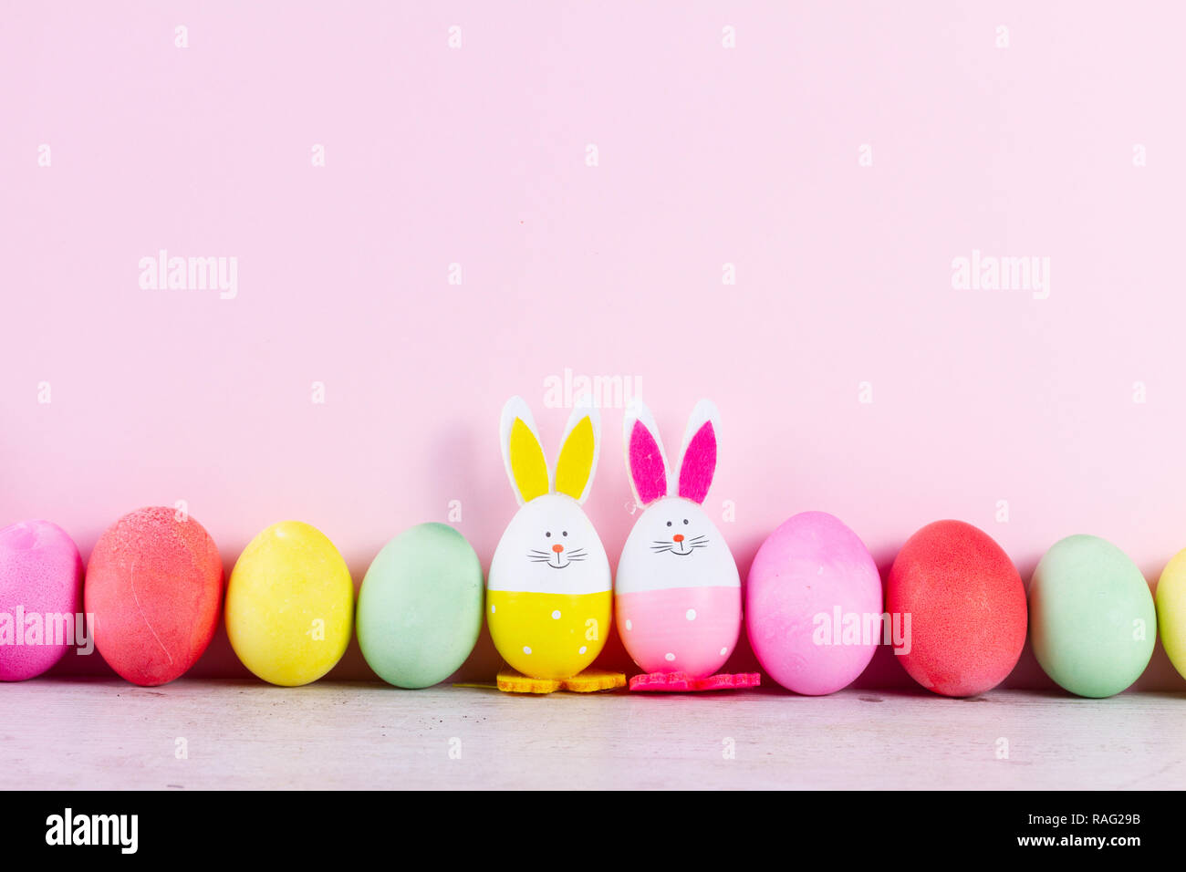 Fila di divertenti conigli pasquali e colorate le uova di pasqua di pastello su sfondo rosa con spazio di copia Foto Stock