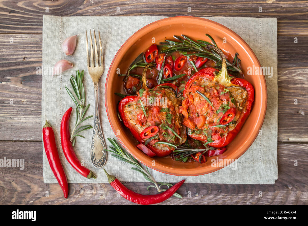 Farcite peperone rosso piccante con salsa di pomodoro e il rosmarino nel piatto di argilla al rustico sfondo di legno. Foto Stock