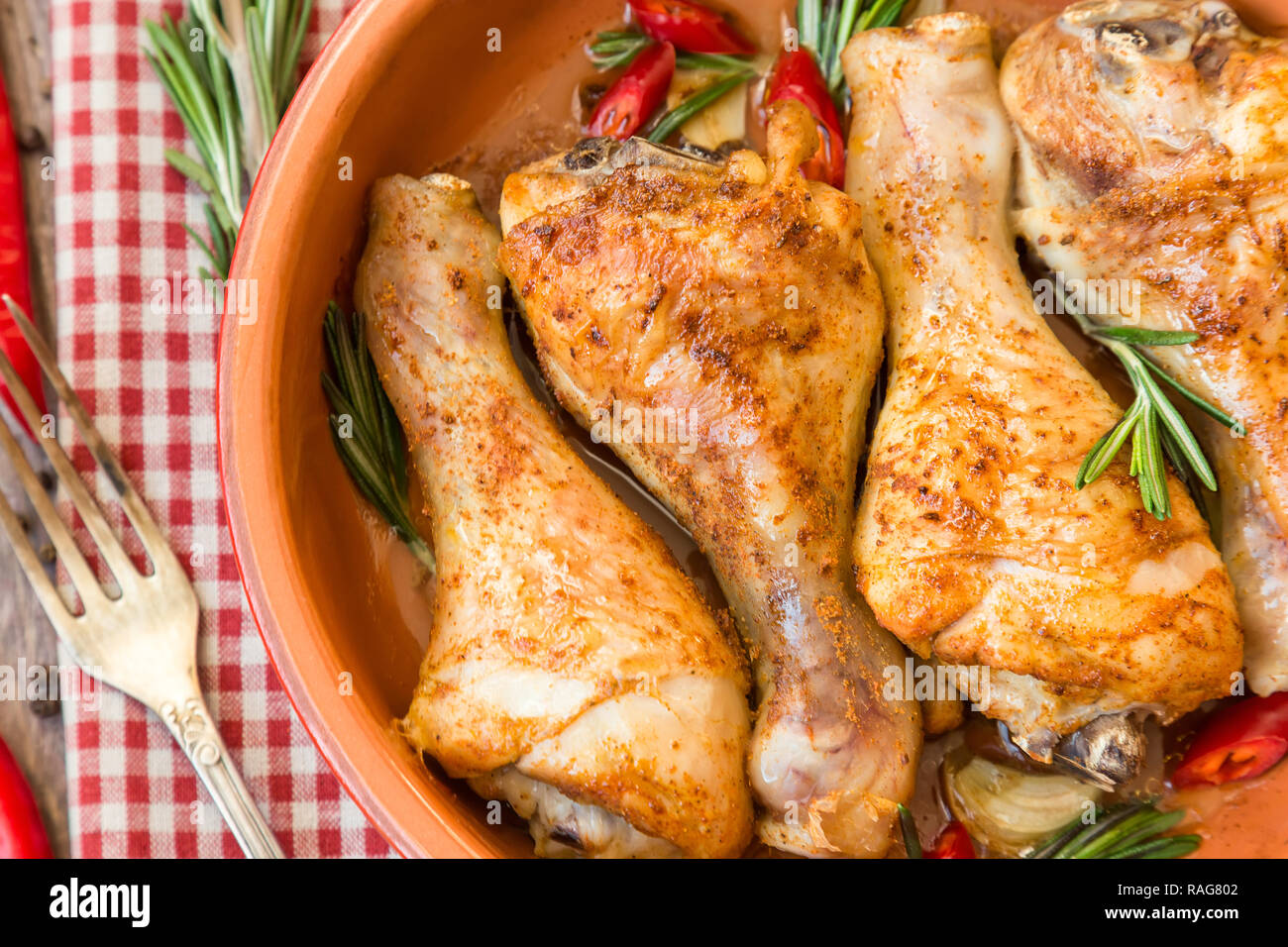 Arrosto di cosce di pollo con rosmarino, aglio e peperoncino rosso in legno rustico sfondo. Vista dall'alto. Messa a fuoco selettiva. Foto Stock