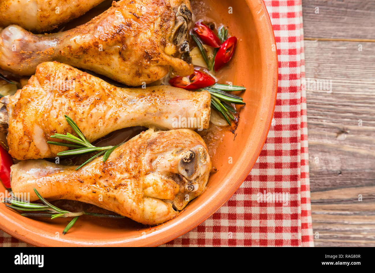 Arrosto di cosce di pollo con rosmarino, aglio e peperoncino rosso in legno rustico sfondo. Vista dall'alto. Foto Stock