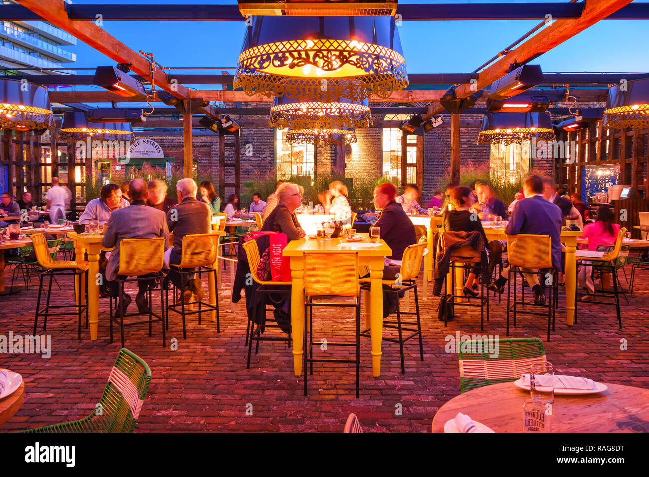 Le persone hanno la cena presso il patio di un ristorante nel quartiere di distilleria di Toronto, Canada come visto dal marciapiede. Foto Stock