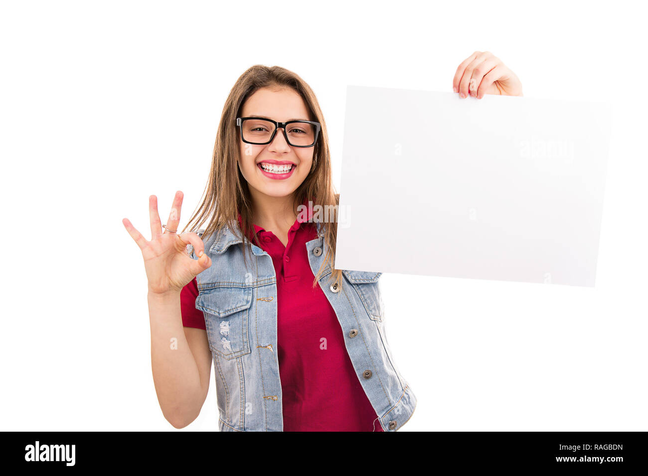 Moderna donna casual in bicchieri tenendo un foglio di carta pulito vuoto e mostra OK segno alla fotocamera su sfondo bianco Foto Stock