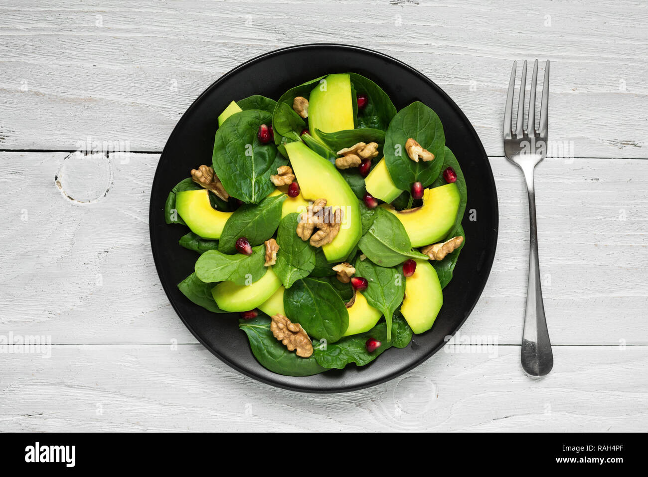 Vegano con insalata di avocado, spinaci, melograno e noci in lamiera nera con la forcella. Il cibo sano. vista superiore Foto Stock