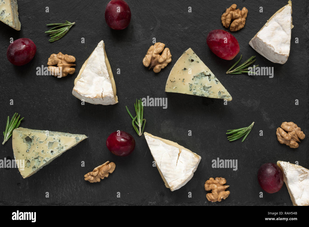 O Camembert Brie e blu le fette di formaggio con uve, noci e di rosmarino su nero ardesia sfondo. vista dall'alto. Una sana prima colazione Foto Stock