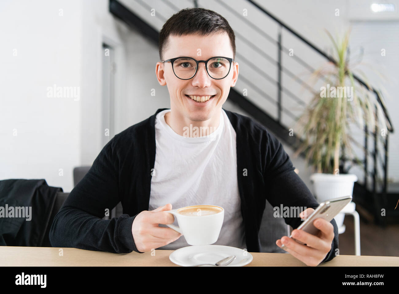 Piscina colpo di giovane uomo sorridente seduto nella caffetteria. Bel ragazzo caucasico presso il cafe utilizzando smart phone. Foto Stock