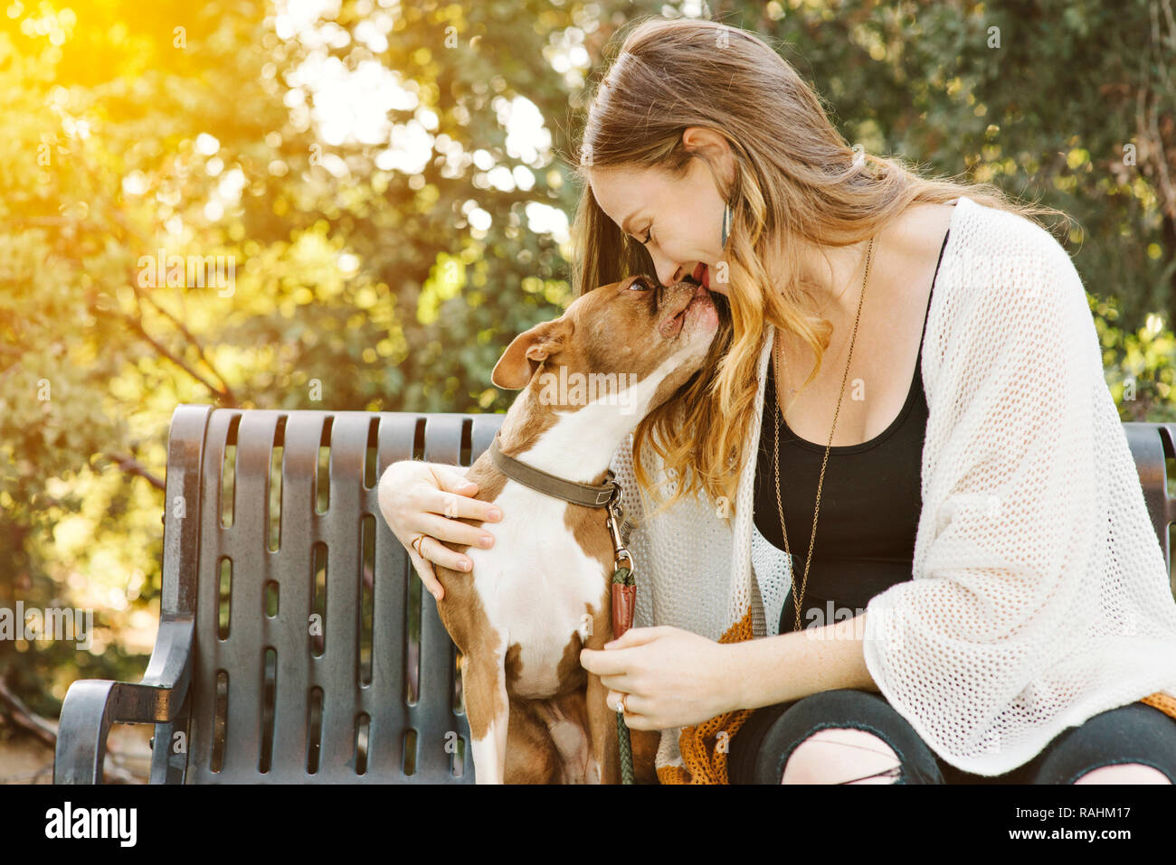 Femmina caucasica con capelli castani bacia il cane su una panchina nel parco. Mans migliore amico. Rapporto amoroso Foto Stock