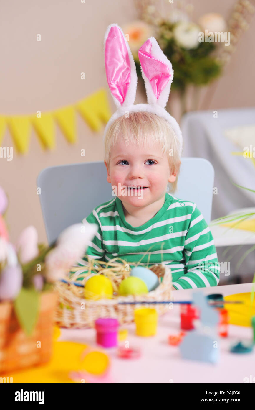Baby boy dipinge le uova in giallo sullo sfondo di una festosa decor a molla Foto Stock