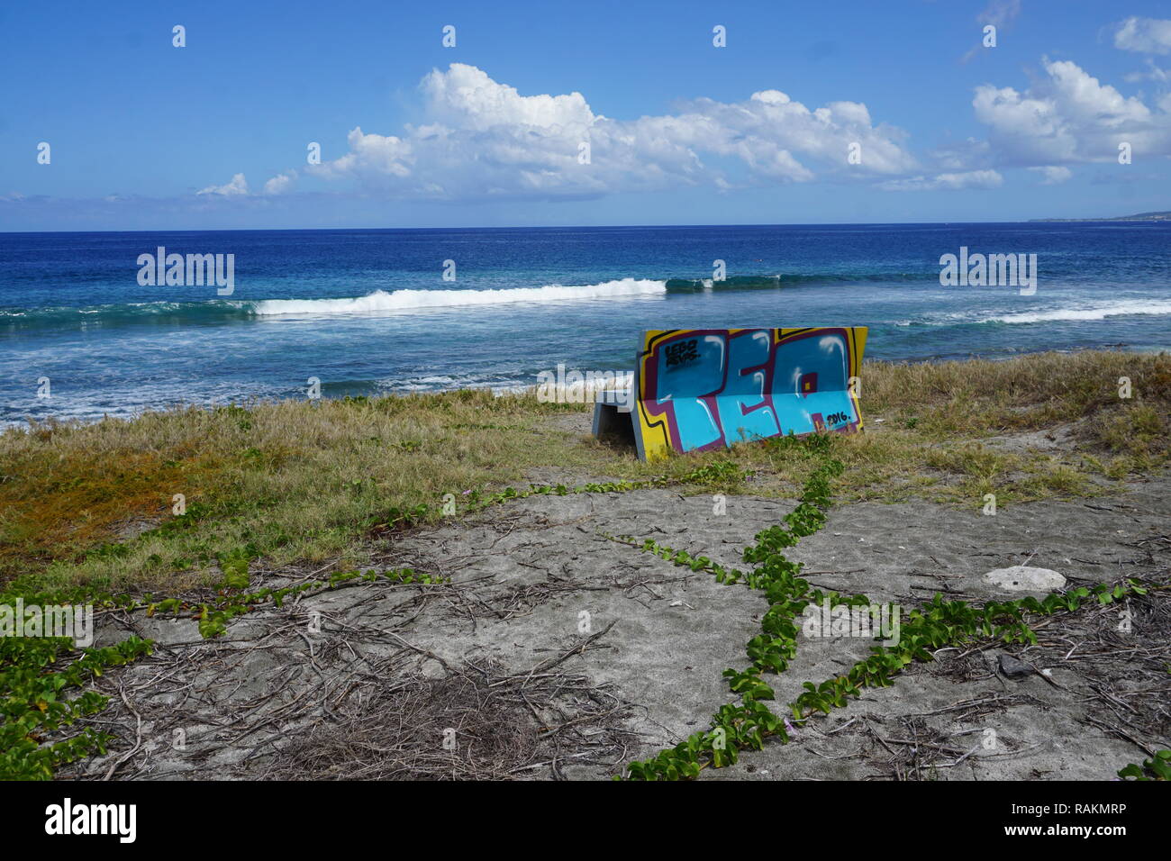 Un lone contrassegnate da banco in pietra con una vista della spiaggia e del mare a La Réunion, Francia in una limpida giornata di blu Foto Stock