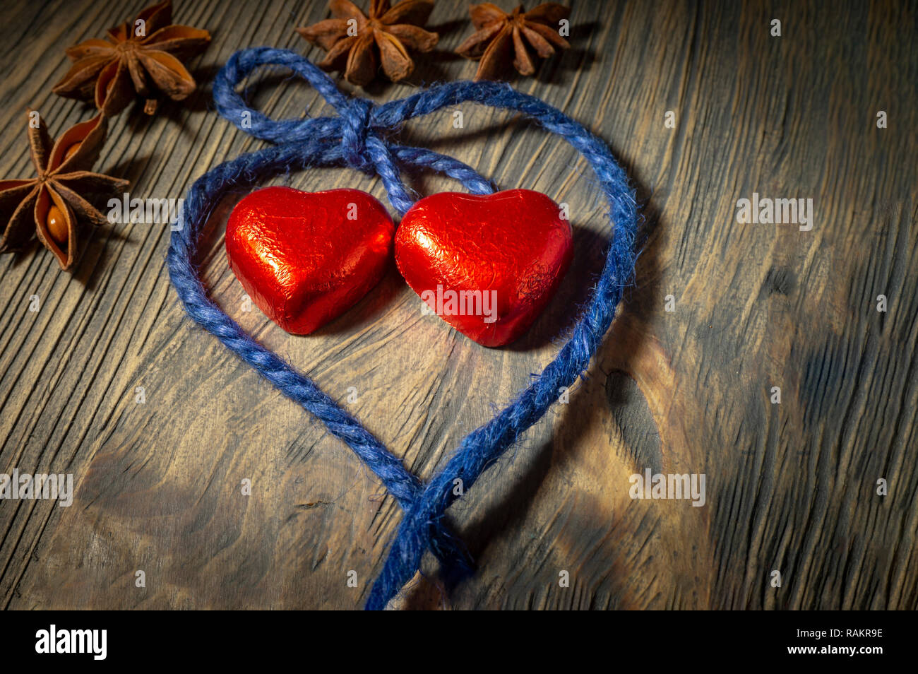 A forma di cuore ad caramelle avvolto in bobina rosso con filetto blu e anice stellato spezie, visto in close-up su sfondo di legno Foto Stock