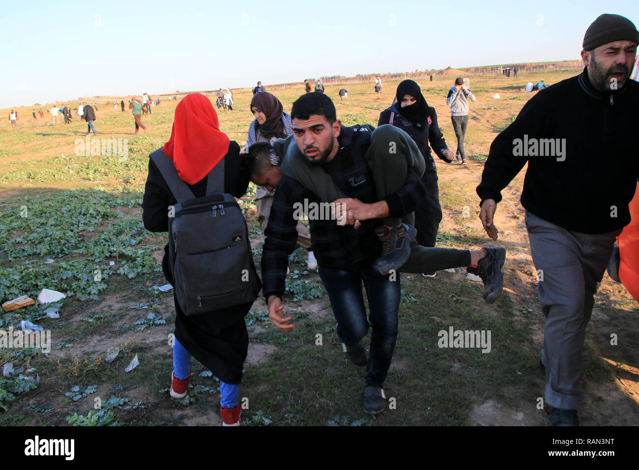 Un uomo visto che trasportano una persona infortunata durante le dimostrazioni tra i cittadini palestinesi e forze di occupazione israeliane nel corso di una protesta contro il riconoscimento del Presidente americano Trump Gerusalemme come capitale di Israele ha rifiutato il blocco del nord della Striscia di Gaza. Foto Stock