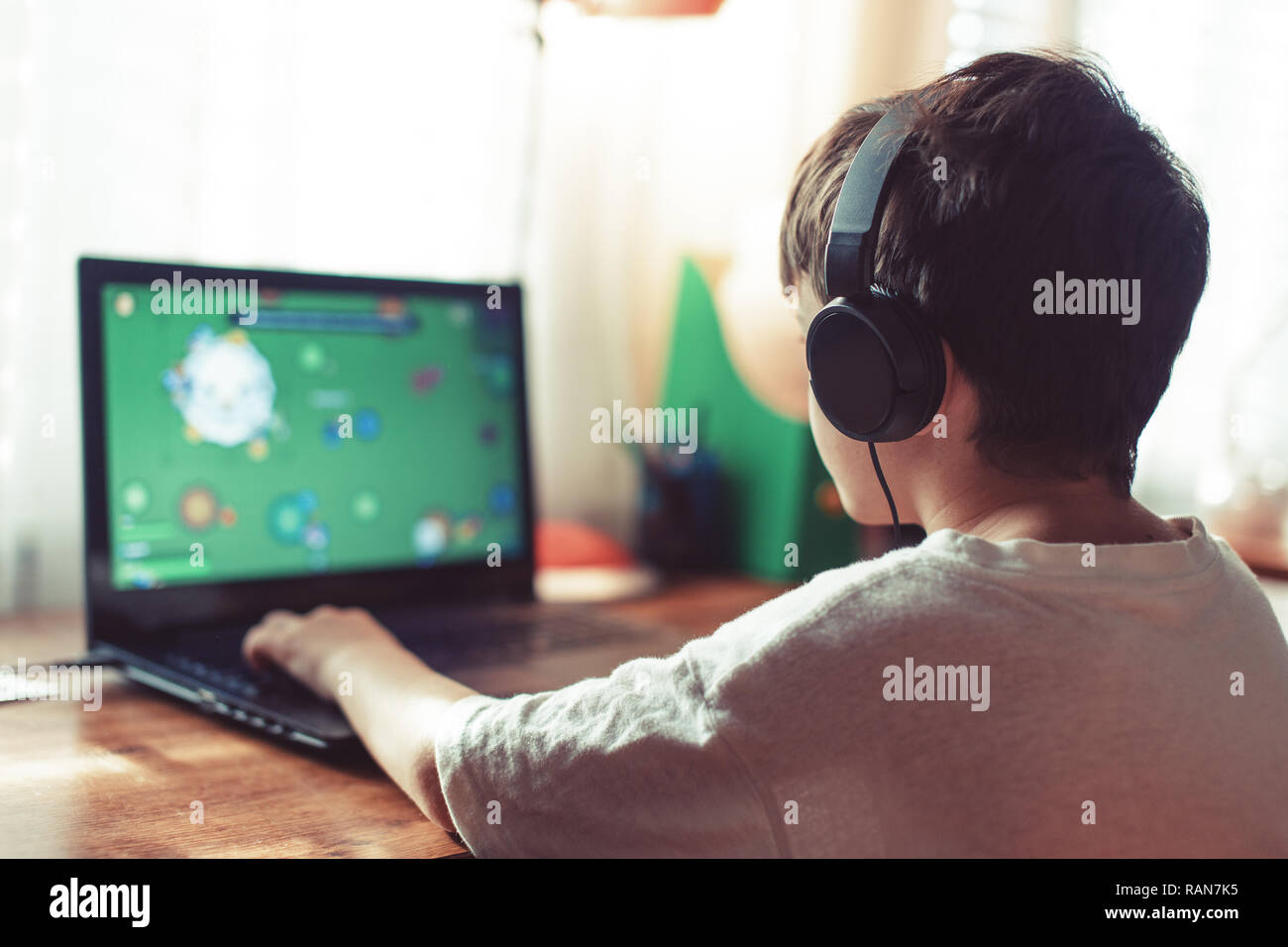 Poco dipendente Ragazzo giocatore a giocare sul computer portatile per interni Foto Stock
