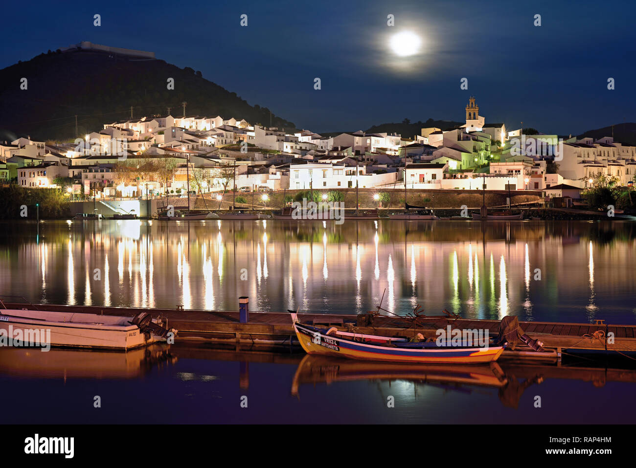 Romantico bianco lavato riverside village con la luna e il legno barche da pesca l'ancoraggio al quay (vista dal Portogallo verso la Spagna) Foto Stock