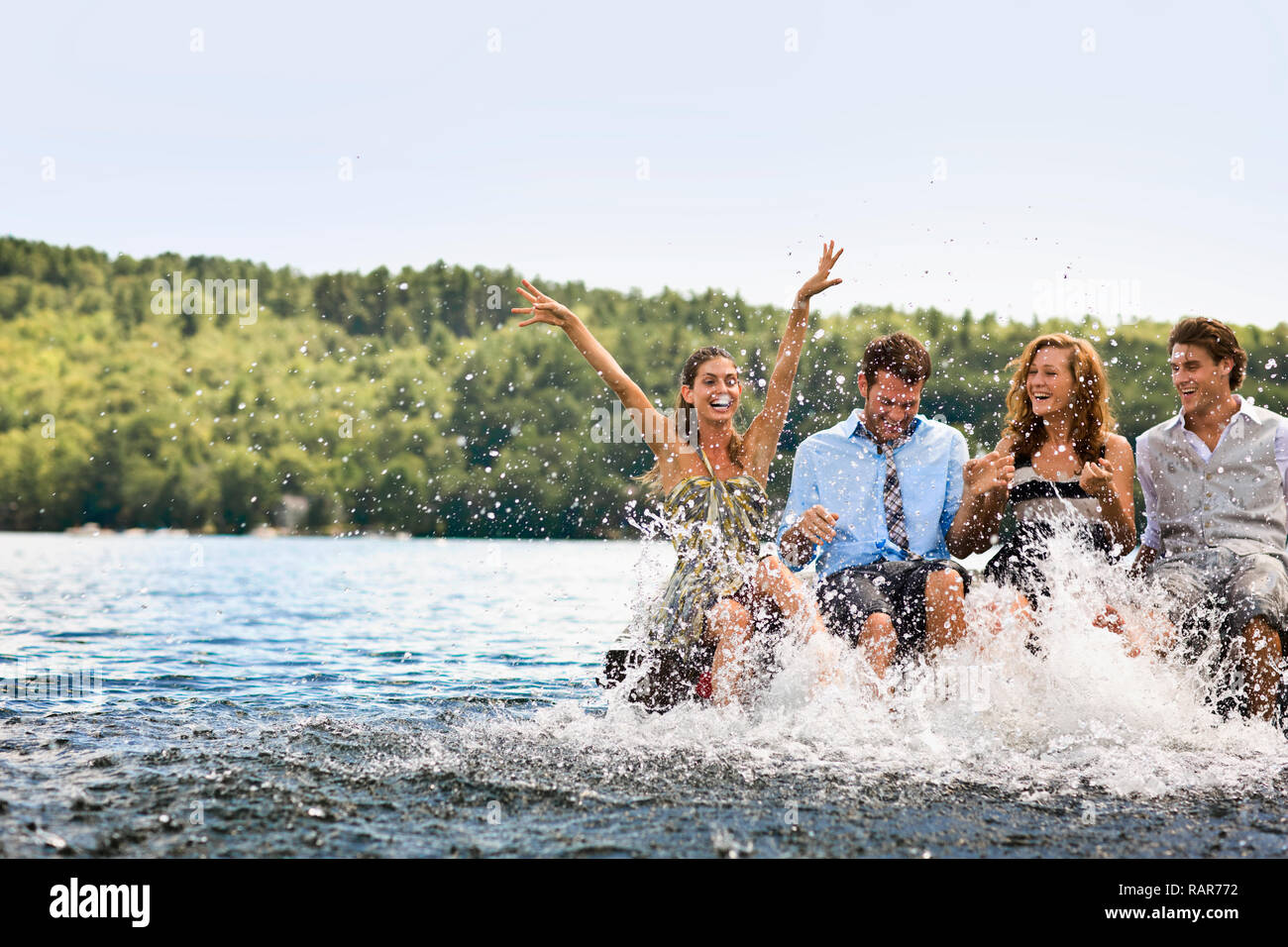 Gruppo di amici seduto su di un molo, schizzi nel lago con le loro gambe. Foto Stock