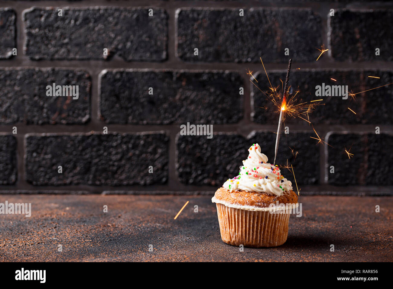 Compleanno tortina con crema e sparkler sul muro di mattoni in background Foto Stock