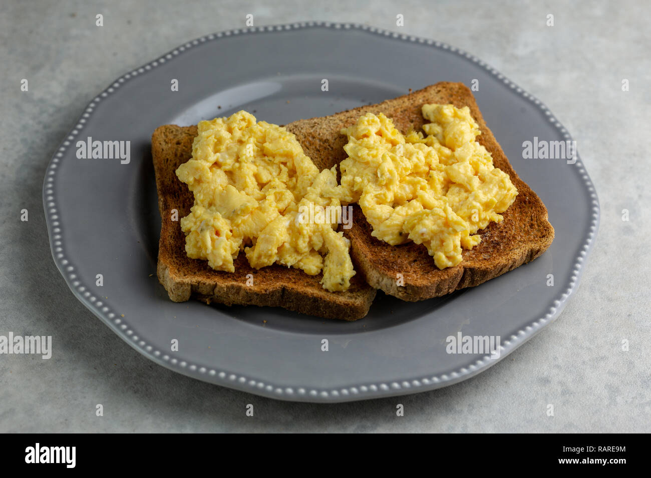 Uova strapazzate su due pezzi di pane tostato su una lastra grigia su una semplice grigio e bianco sullo sfondo di marmo Foto Stock
