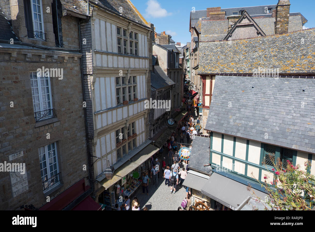 I turisti a piedi su una stretta strada costeggiata da negozi e ristoranti presso il centro storico di Mont Saint-Michel. La Normandia, Francia Foto Stock