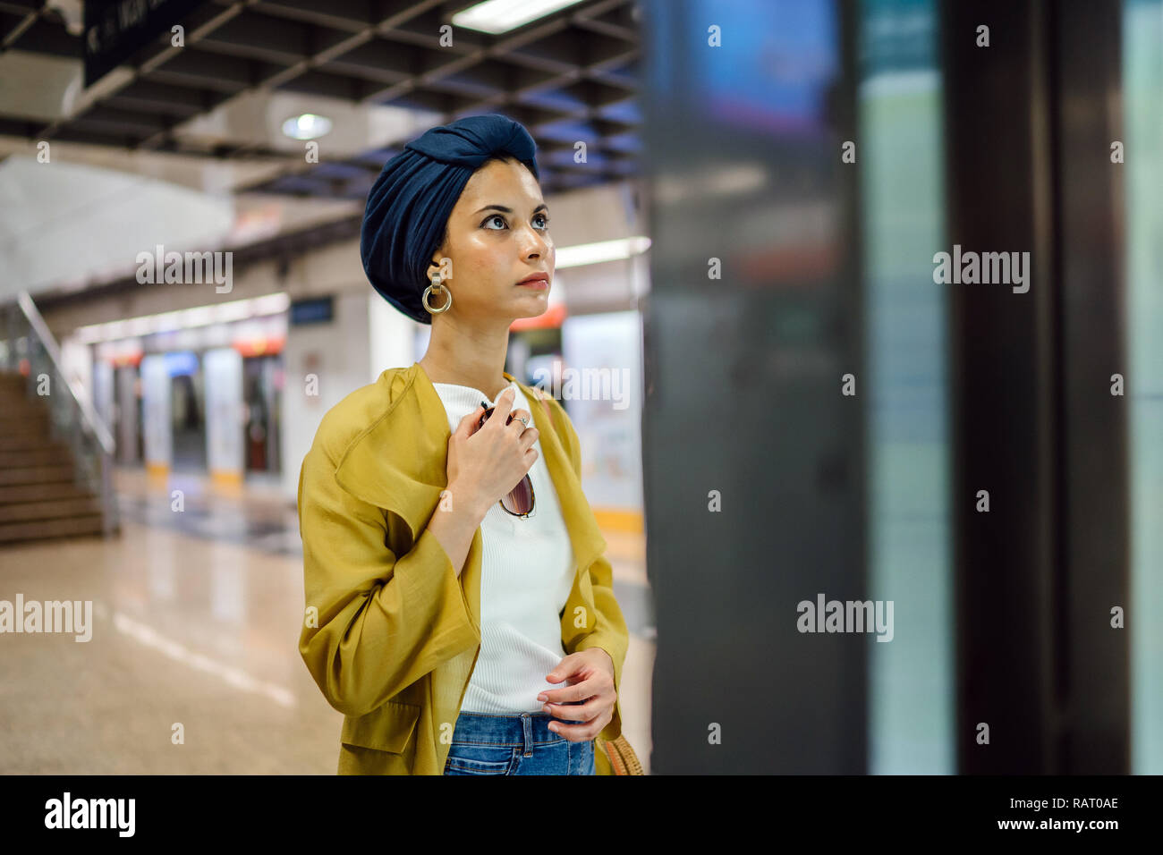 Una giovane e attraente donna musulmana in un velo e elegante color pastello vestiti è la consultazione di una mappa in una stazione ferroviaria per raggiungere la sua destinazione. Foto Stock