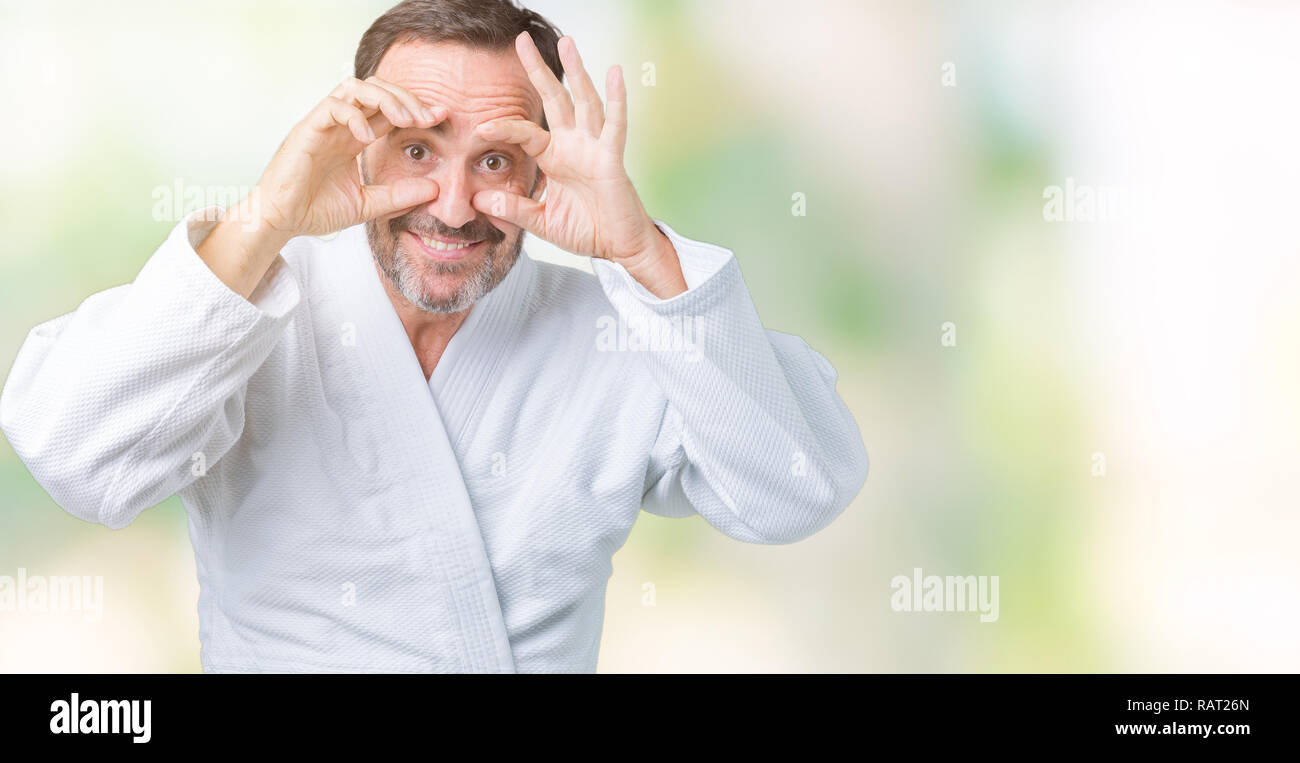 Bella la mezza età senior uomo indossare il kimono uniforme su sfondo isolato cercando di aprire gli occhi con le dita, assonnato e stanco per la fatica di mattina Foto Stock