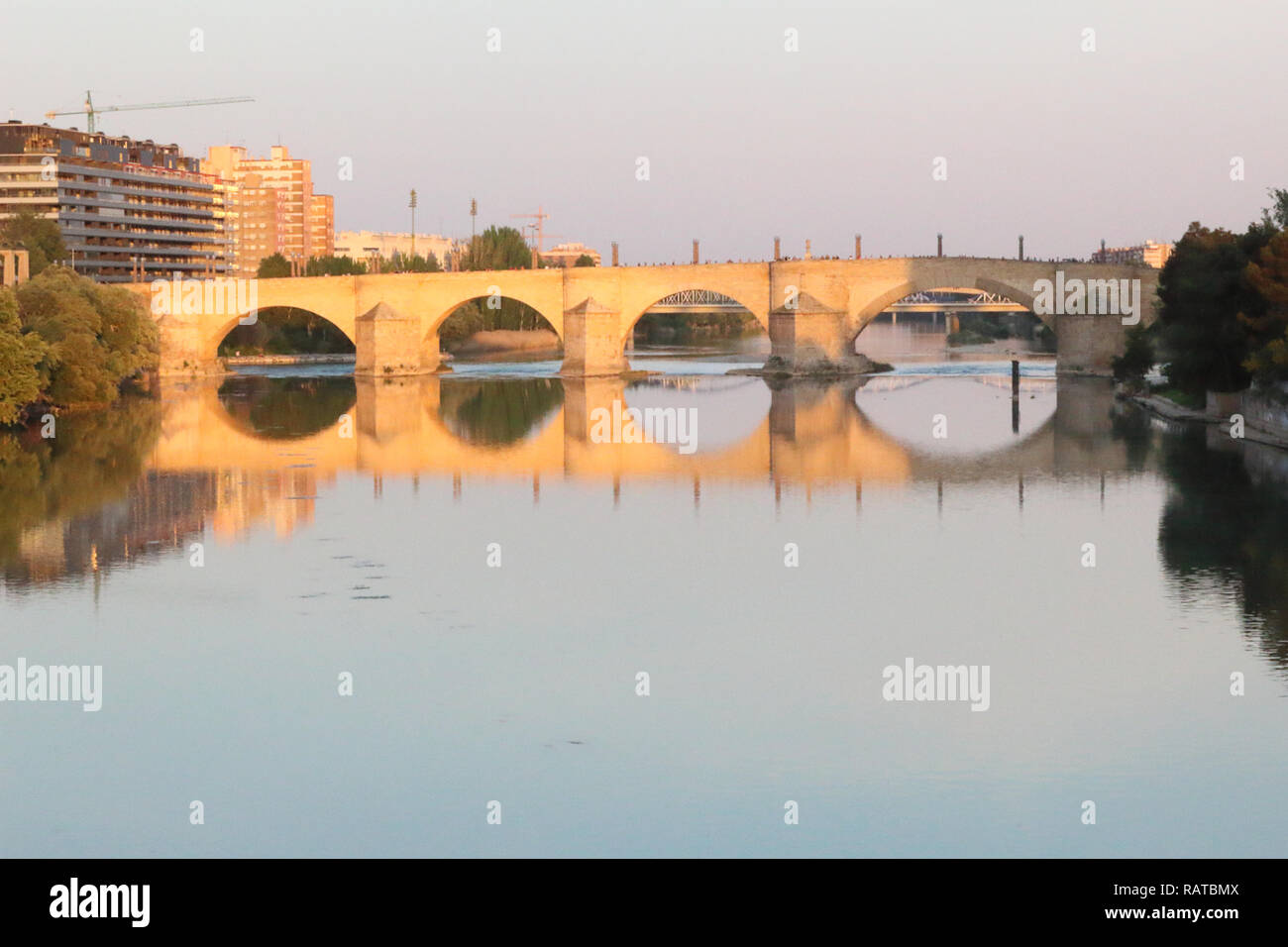 Il Puente de Piedra ponte in pietra con archi a tutto sesto che riflette nel grande fiume Ebro acque al tramonto a Saragozza, regione di Aragona, Spagna Foto Stock
