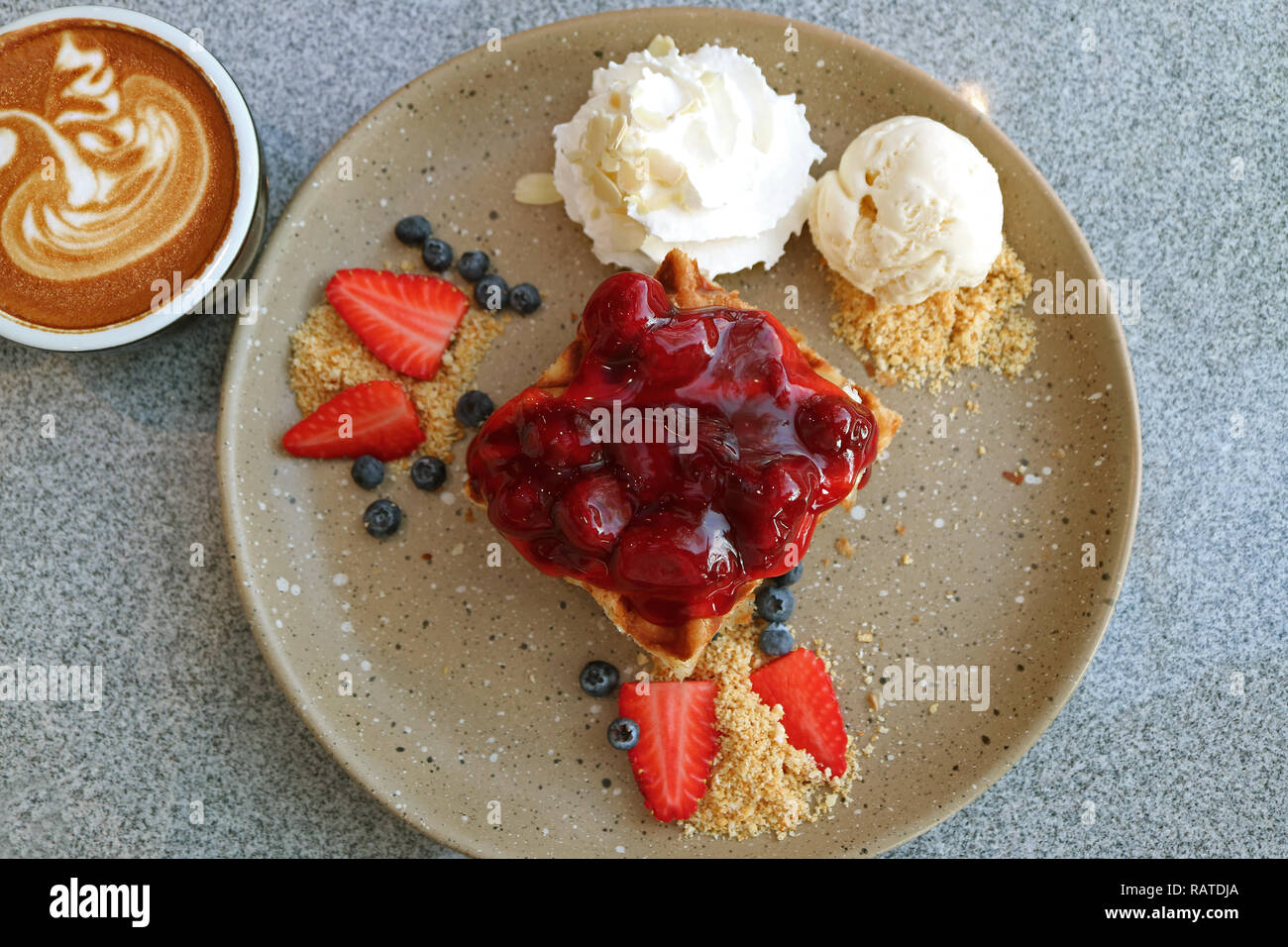 Vista superiore della cialda con salsa di fragole, frutti di bosco freschi, gelato alla vaniglia e una tazza calda di caffè cuppuccino Foto Stock
