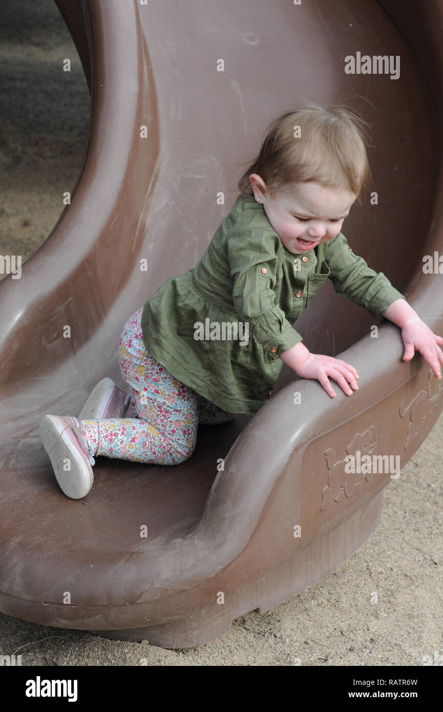 Un anno di età su una diapositiva in un parco giochi Foto Stock