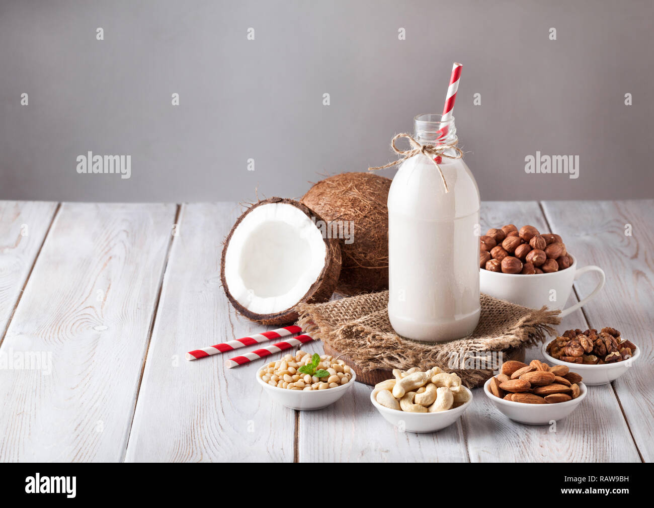 Latte vegano da dadi nella bottiglia con red spogliato paglia intorno vari dadi bianco sul tavolo di legno Foto Stock