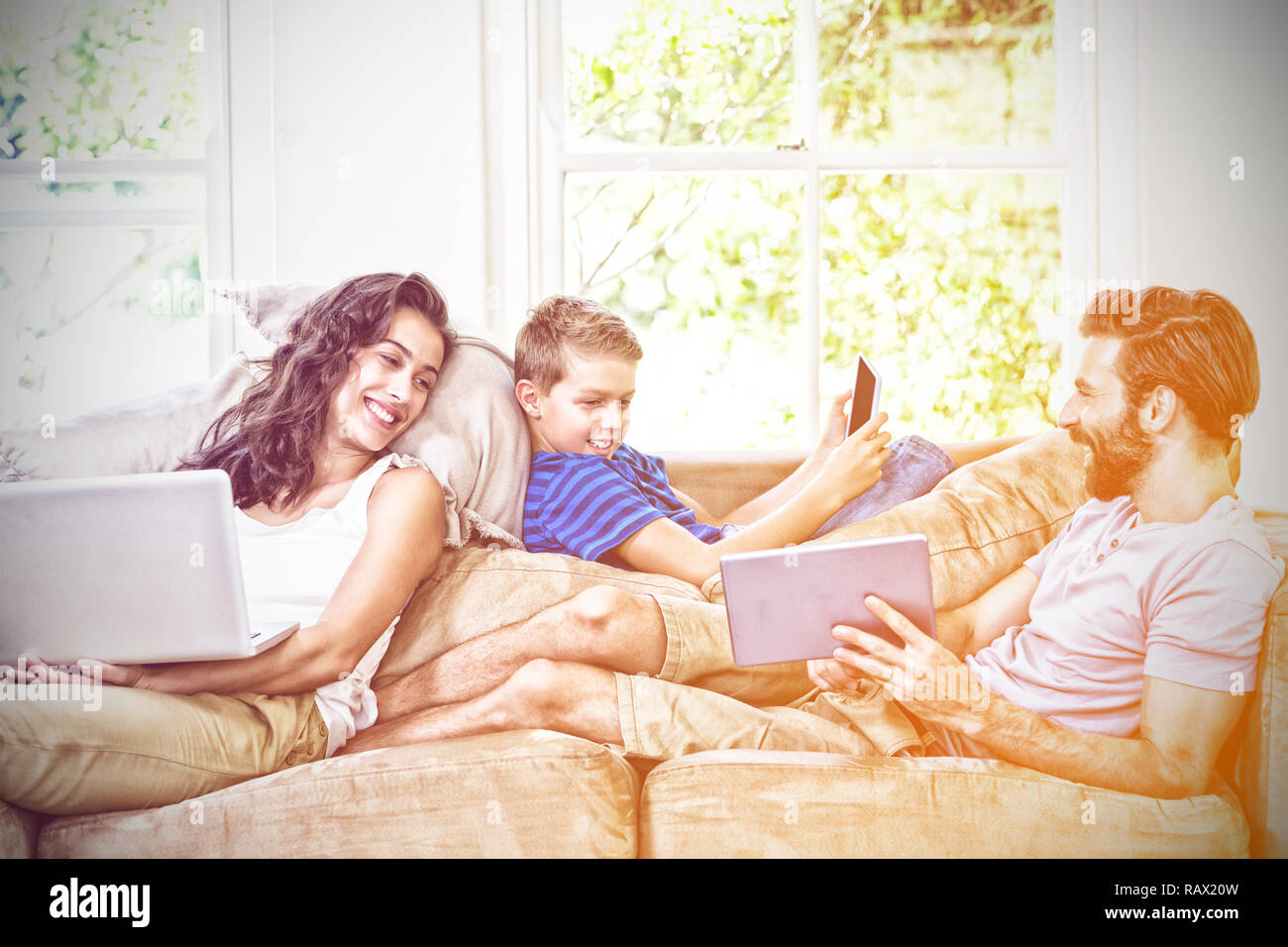 Famiglia allegra utilizzando tecnologie sdraiati sul divano Foto Stock