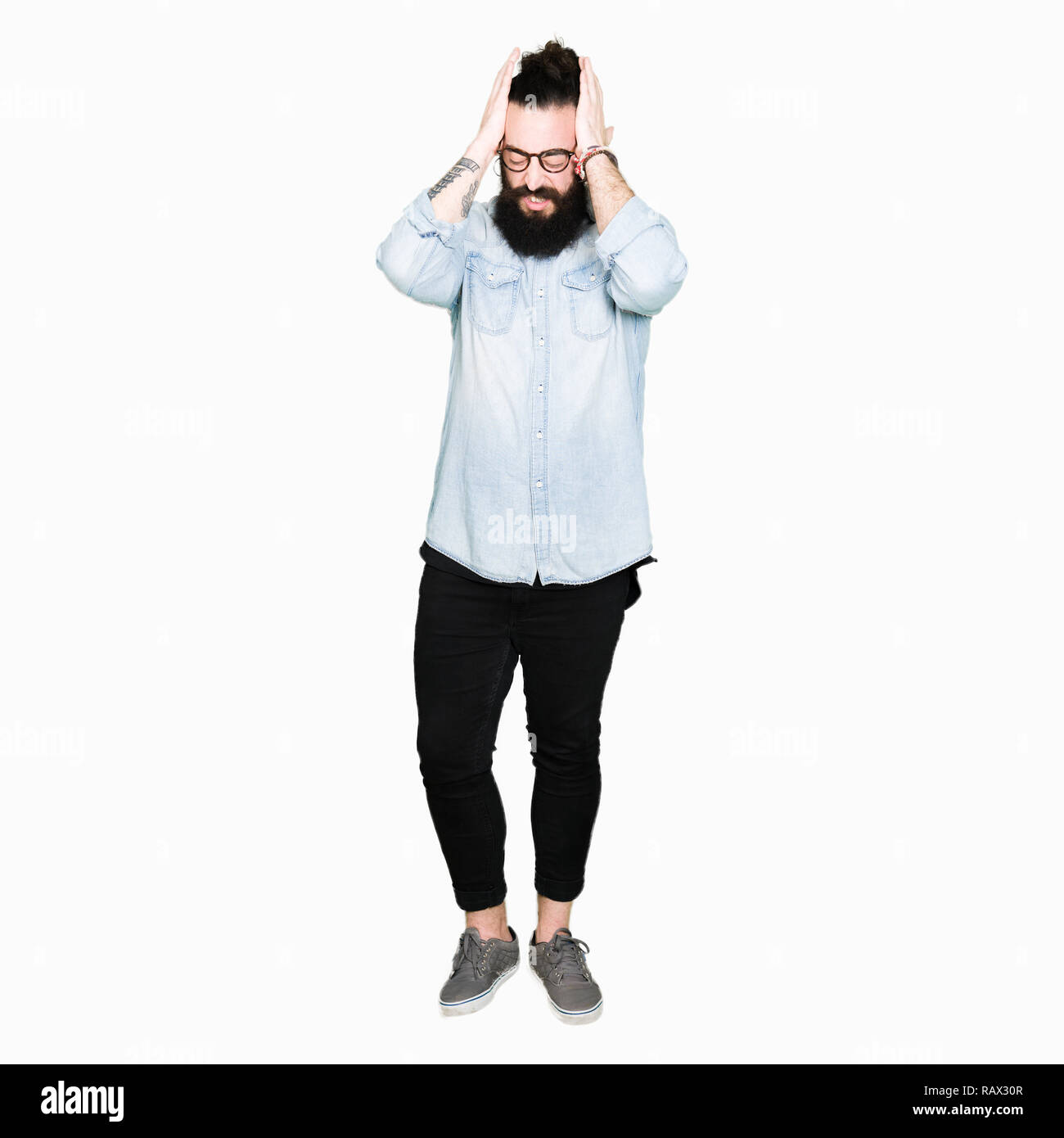 Tanga giovane uomo con i capelli lunghi e la barba con gli occhiali che soffrono di mal di testa disperato e ha sottolineato perché il dolore e l'emicrania. Mani sulla testa. Foto Stock