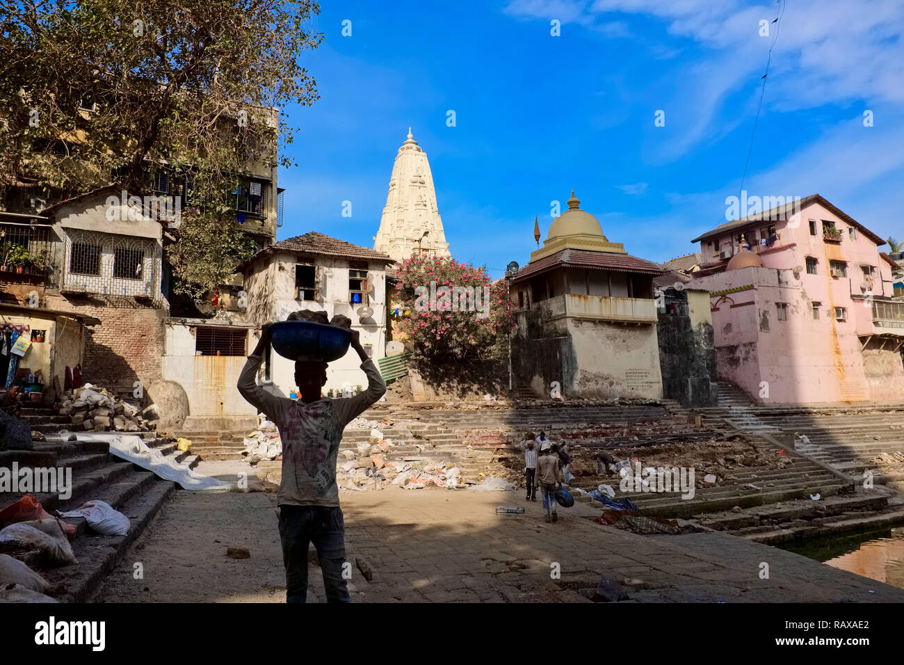 Un lavoratore di rinnovamento a Banganga serbatoio, un tempio sacro sito in Mumbai, India, trasportare laterizi sulla sua testa, che appaiono quasi come una silhouette Foto Stock