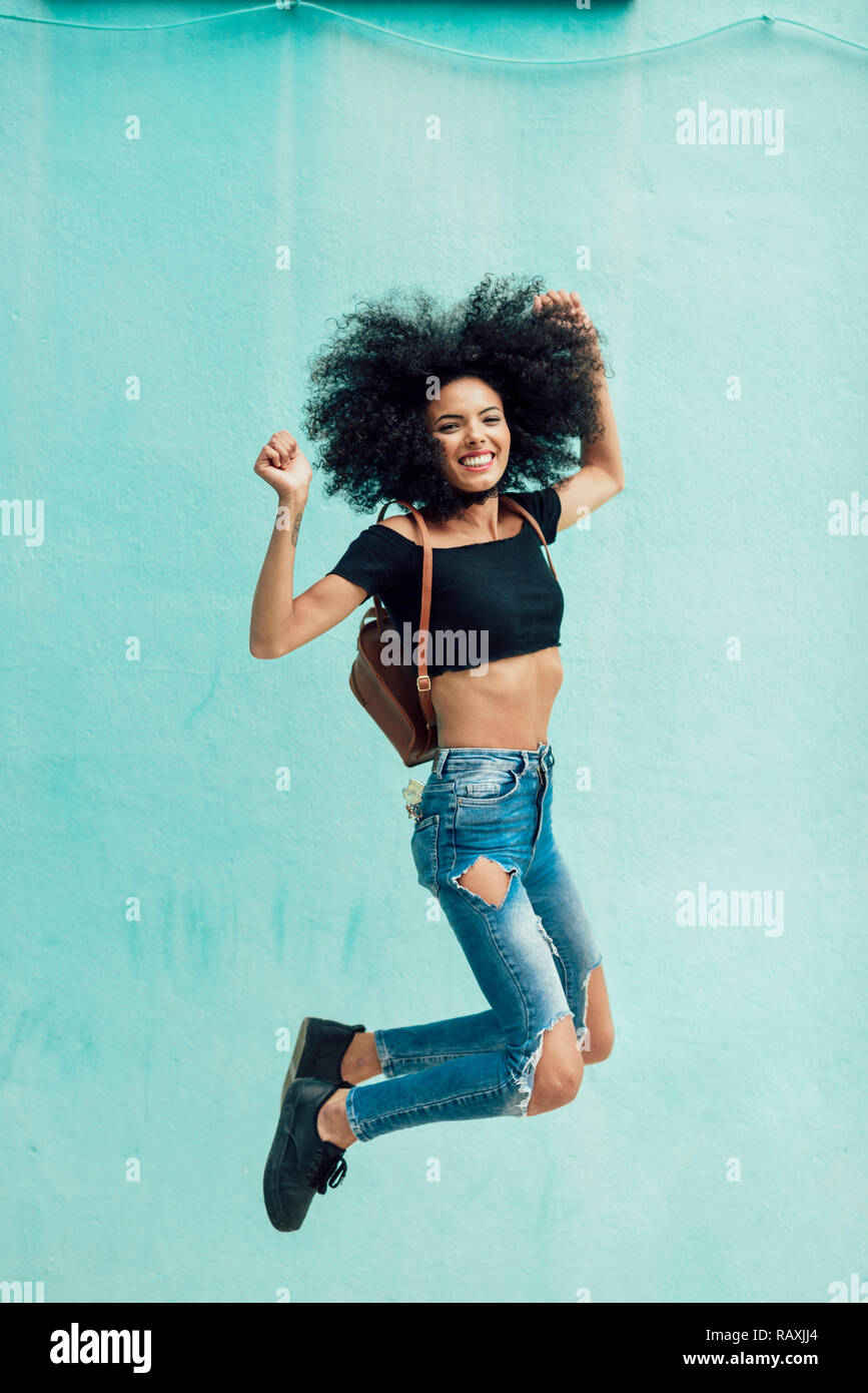 Giovane donna misti con capelli afro jumping all'esterno. Femmina di indossare abiti casual in background urbano. Il concetto di stile di vita Foto Stock