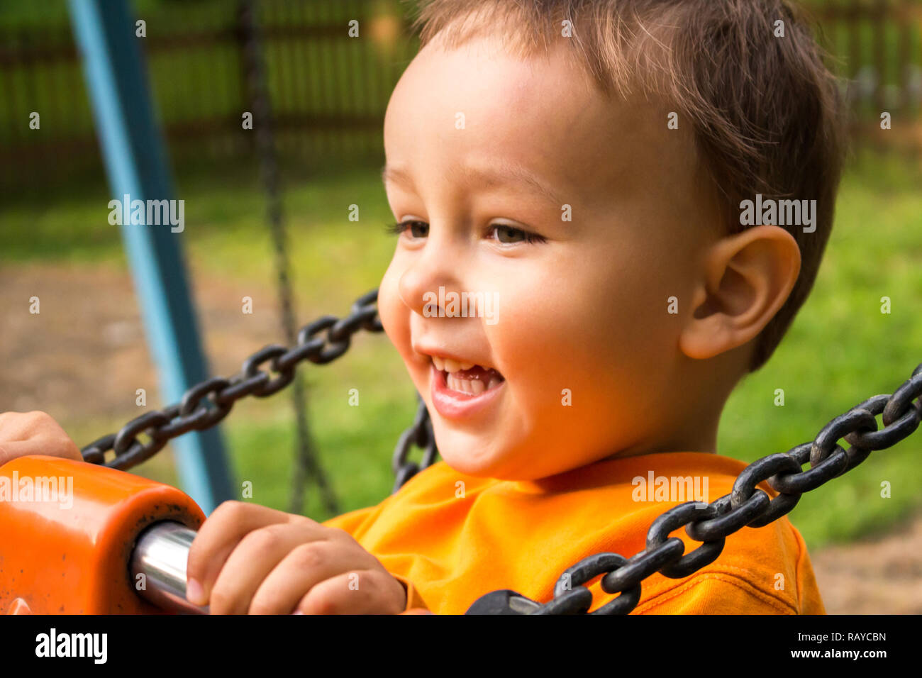 Ragazzo in maglietta arancione su swing sorridente. DOF poco profondo. Foto Stock