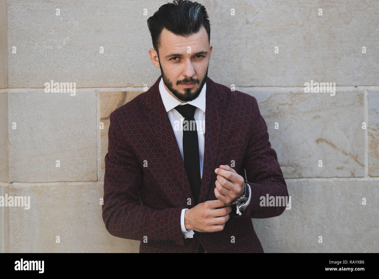 I giovani e la moda uomo abbottonatura un bracciale e in posa all'aperto su un muro di pietra sullo sfondo Foto Stock