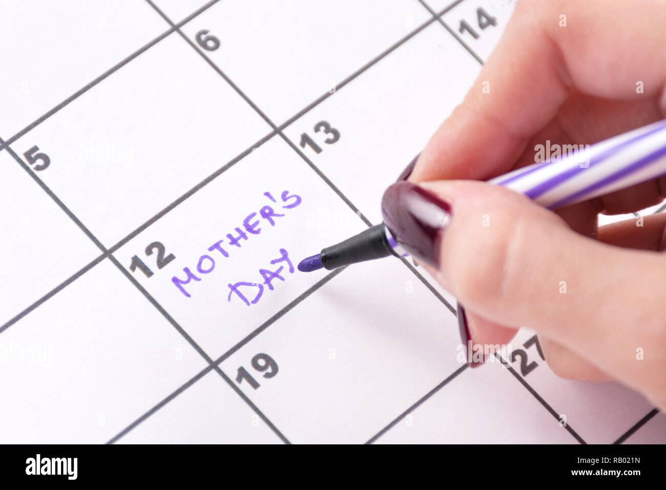 Ragazza con le mani viola pennarello iscritto nel calendario parole madri giorno per vacanza promemoria. Close up, il fuoco selettivo Foto Stock