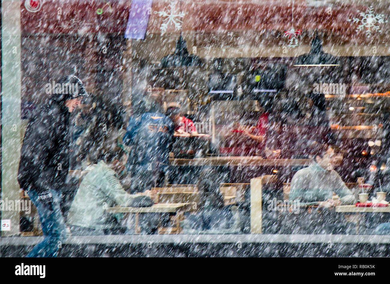 A Belgrado, in Serbia - Dicembre 15, 2018: sfocata uomo a camminare da sola strada di città in forte nevicata e la gente seduta in un ristorante finestra dietro di lui Foto Stock