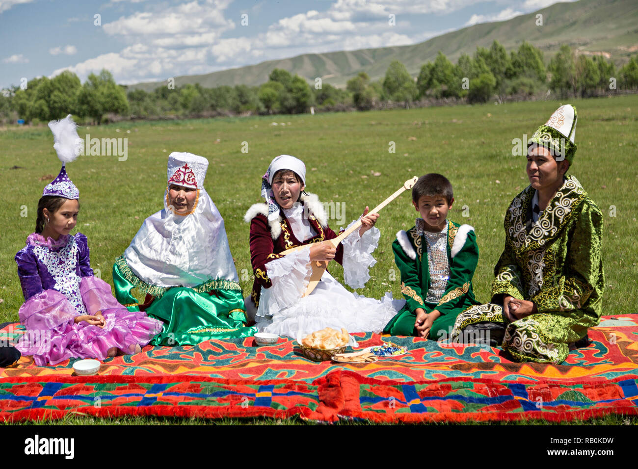 Famiglia kazako in abiti tradizionali con una donna cantare e suonare strumento locale di dombra, Kazakistan. Foto Stock