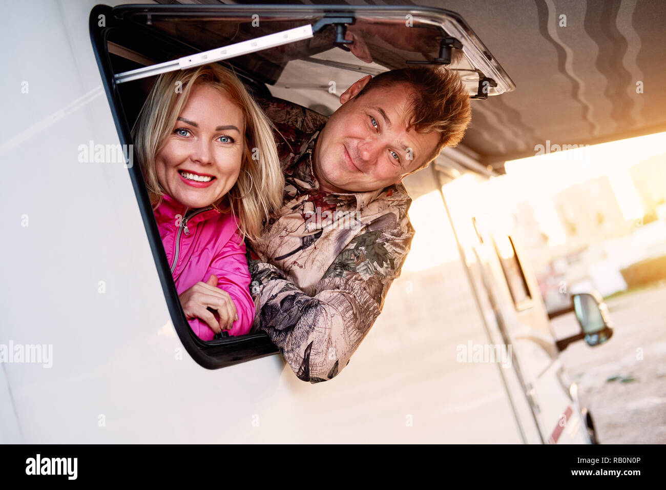 Sposati di mezza età giovane famiglia moglie e marito uscendo dalla roulotte veicolo ricreativo motor home finestra rimorchio guardando la fotocamera Foto Stock