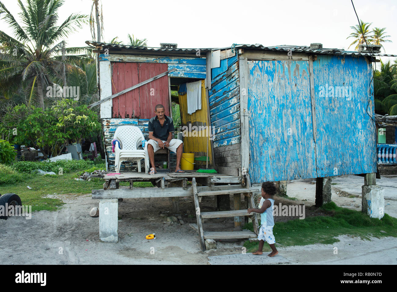 Latino uomo seduto al di fuori della sua casa, vicino a waterfront. Caraibi capanna di legno. Ritratto ambientale, uso editoriale. San Andrés, Colombia. Ott 2018 Foto Stock