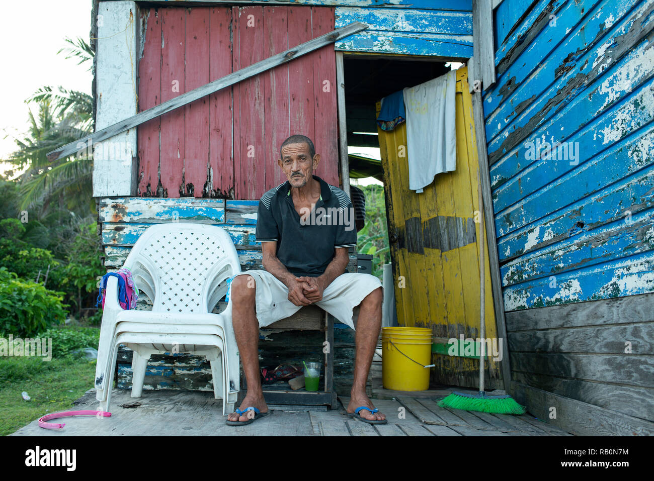 Latino uomo seduto al di fuori della sua casa, vicino a waterfront. Caraibi capanna di legno. Ritratto ambientale, uso editoriale. San Andrés, Colombia. Ott 2018 Foto Stock