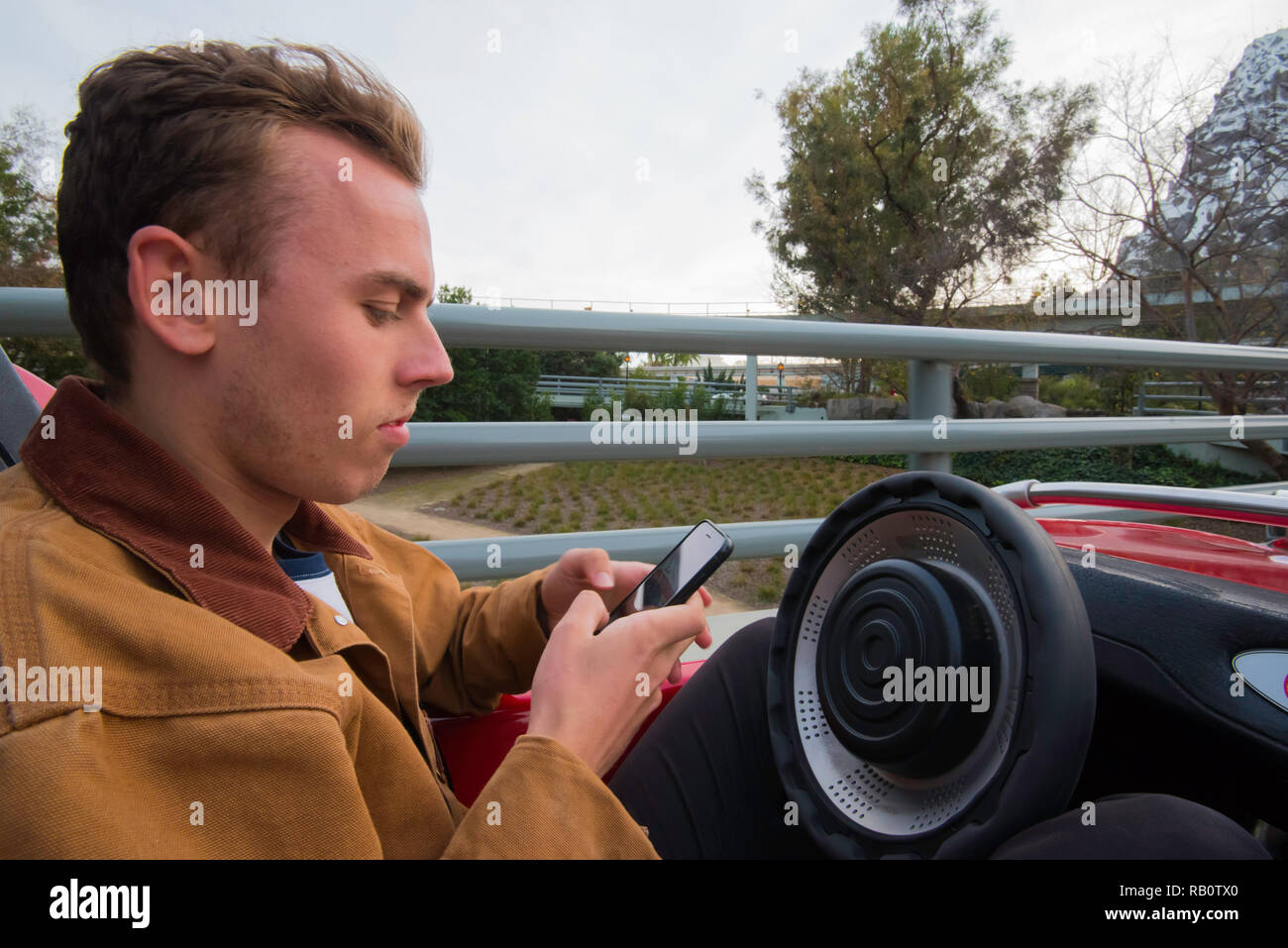 Un giovane maschio gioventù texting mentre si guida una macchina giocattolo a Disneyland Anaheim, LA, California USA Foto Stock