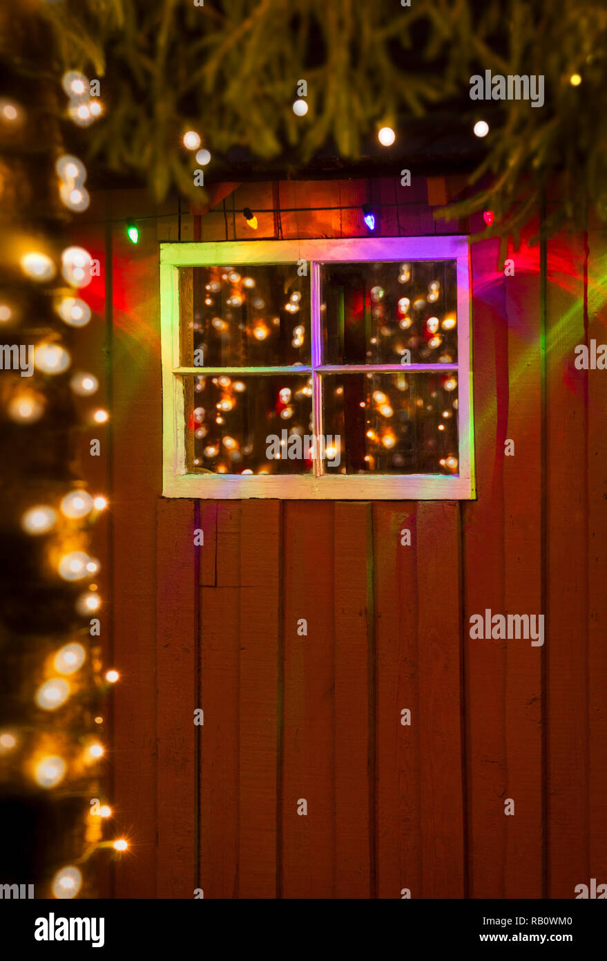 Coloratissima favola di Natale luci di notte si riflette in vetro antico dei riquadri della finestra rustico sul lato di un dipinto di rosso cabina di bosco. Foto Stock