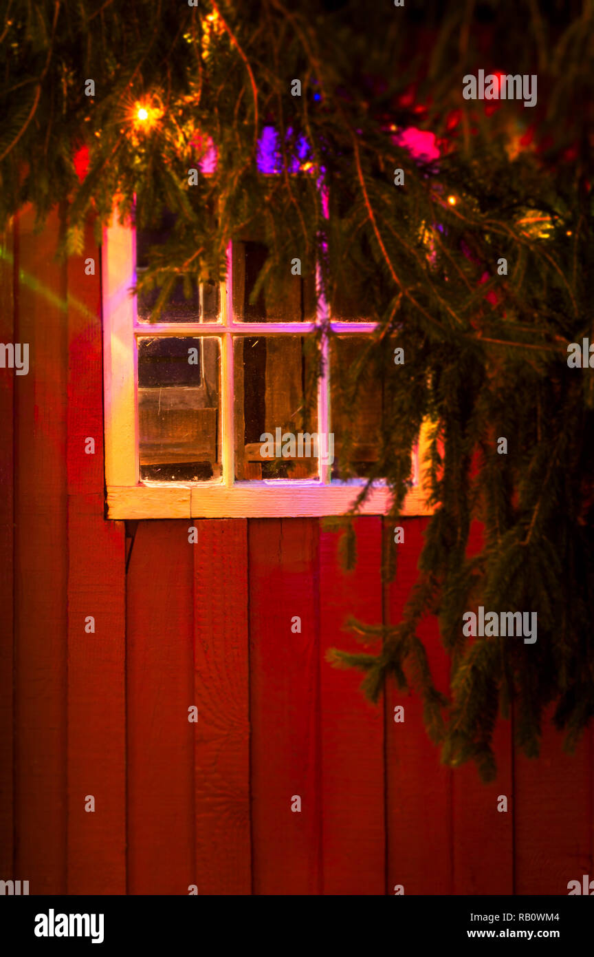 Coloratissima favola di Natale luci di notte si riflette in vetro antico dei riquadri della finestra rustico sul lato di un dipinto di rosso cabina di bosco. Foto Stock