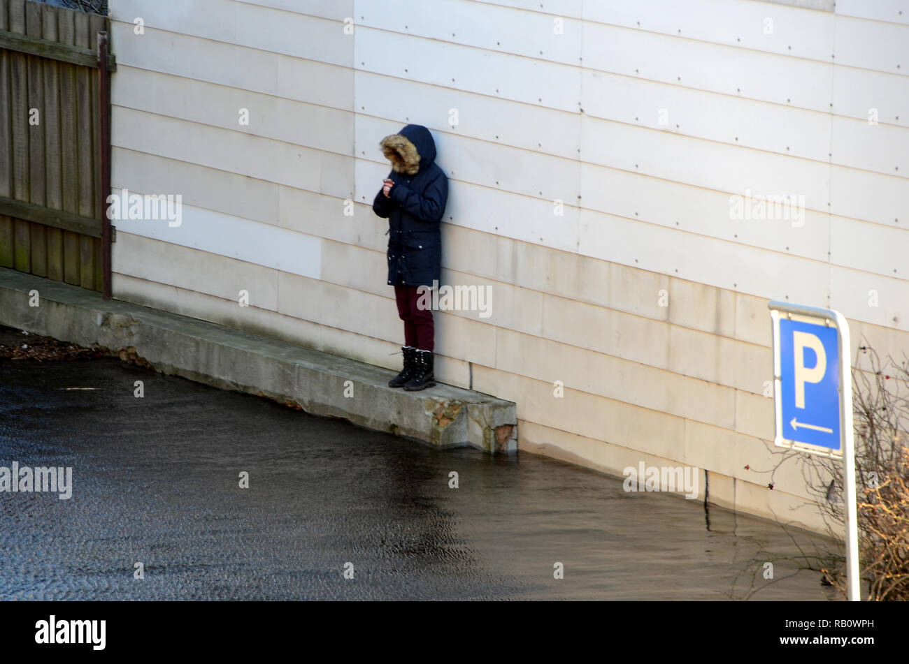 Un ragazzo si erge su uno zoccolo in calcestruzzo, guardando l'acqua su una superficie allagata parcheggio. Foto Stock