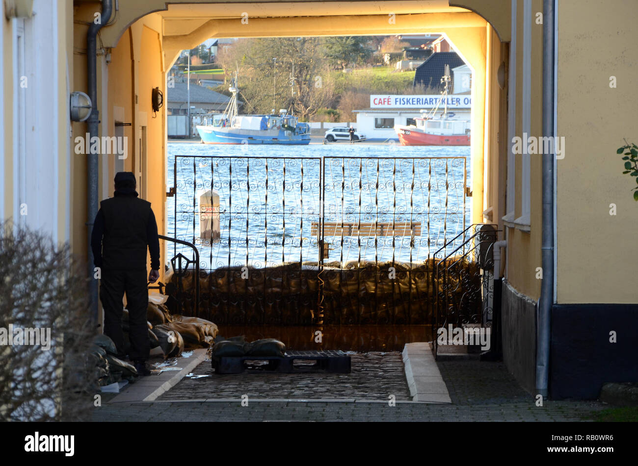 Sonderborg, Danimarca - 2 Gennaio 2019: uomo anziano si affaccia su una mareggiata attraverso un cancello protetto con sacchi di sabbia. Foto Stock