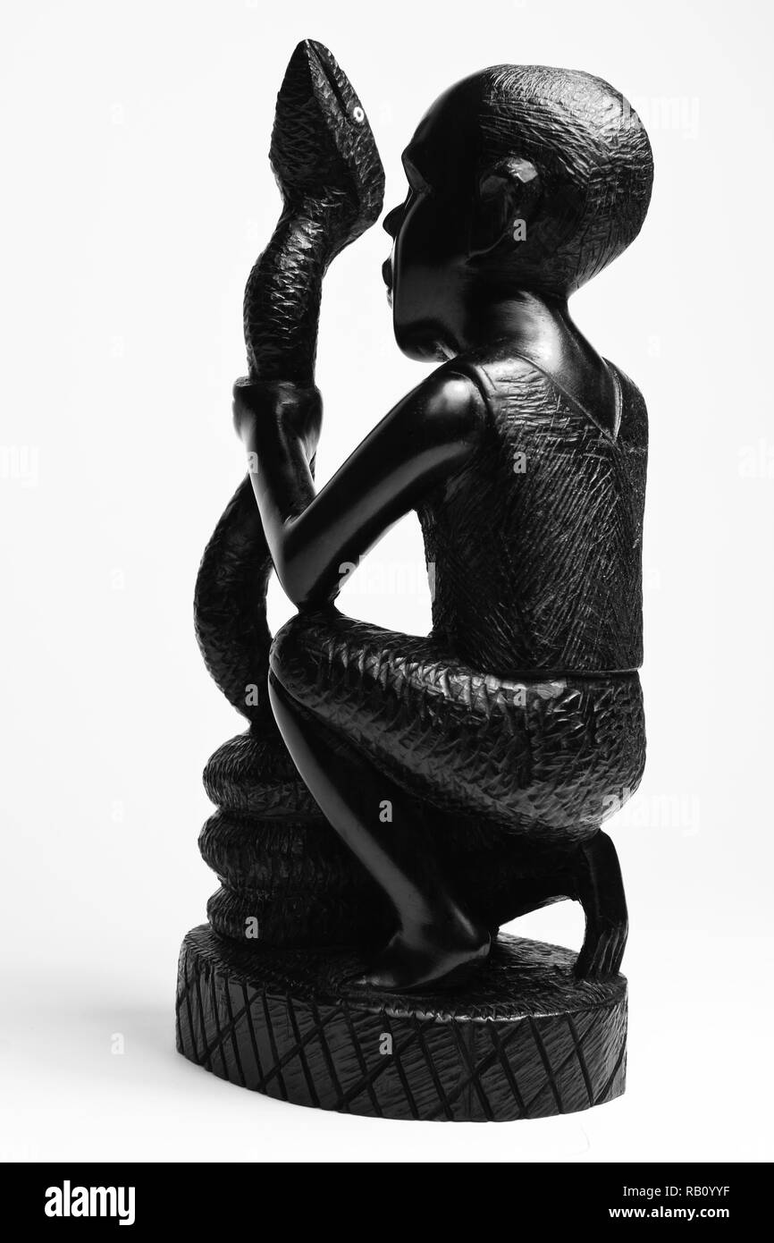 In legno figura africana ferro arte scultura in legno scultura. L'uomo, in squatting posizione sollevata la mano e tenendo il serpente. 8 × 7 × 9 cm. Da dietro. Foto Stock