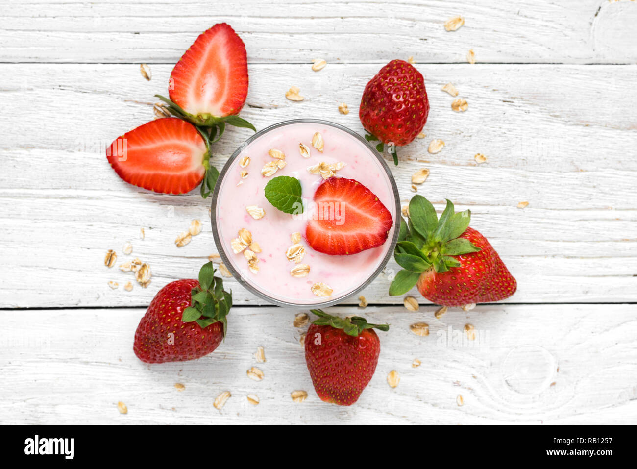 Yogurt alla fragola in un vetro con frutti di bosco freschi, avena e menta bianca su sfondo di legno. Colazione sana. vista superiore Foto Stock