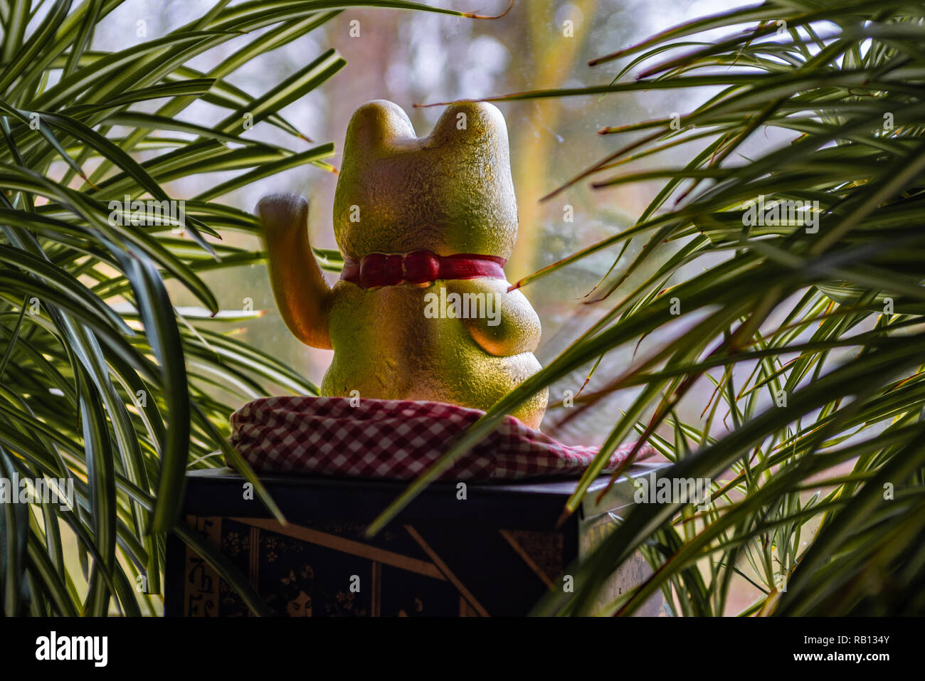 Close up di un cinese golden fortune cat (Maneki Neko) su un davanzale tra piante Foto Stock