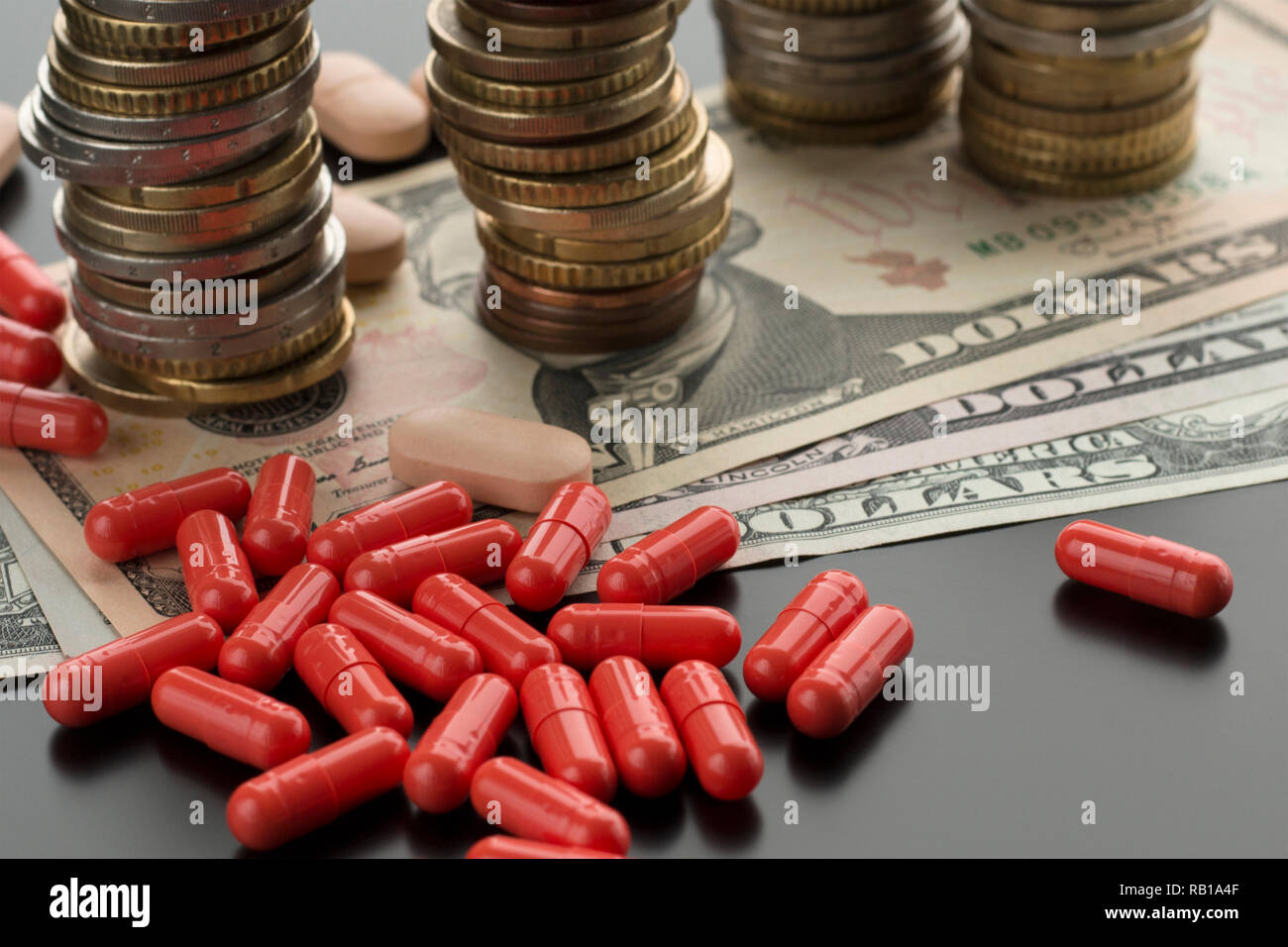 Red pillole o capsule e dollaro banconote, pile di monete sullo sfondo. Argomento delle spese mediche nel bilancio di famiglia, la cura della salute Foto Stock
