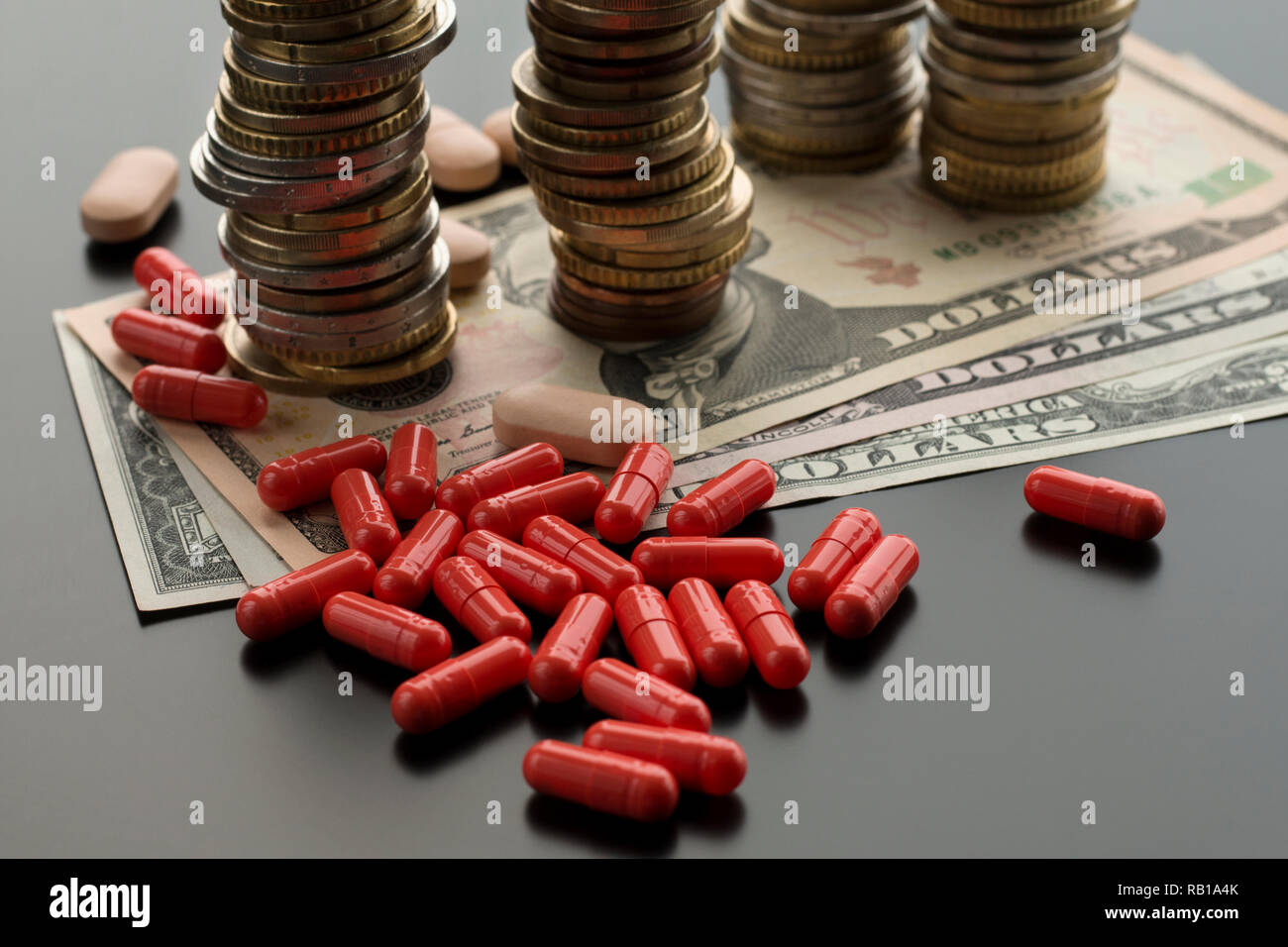 Red pillole o capsule contro le fatture del dollaro e pile di monete su sfondo scuro. Concetto di cure costose Foto Stock