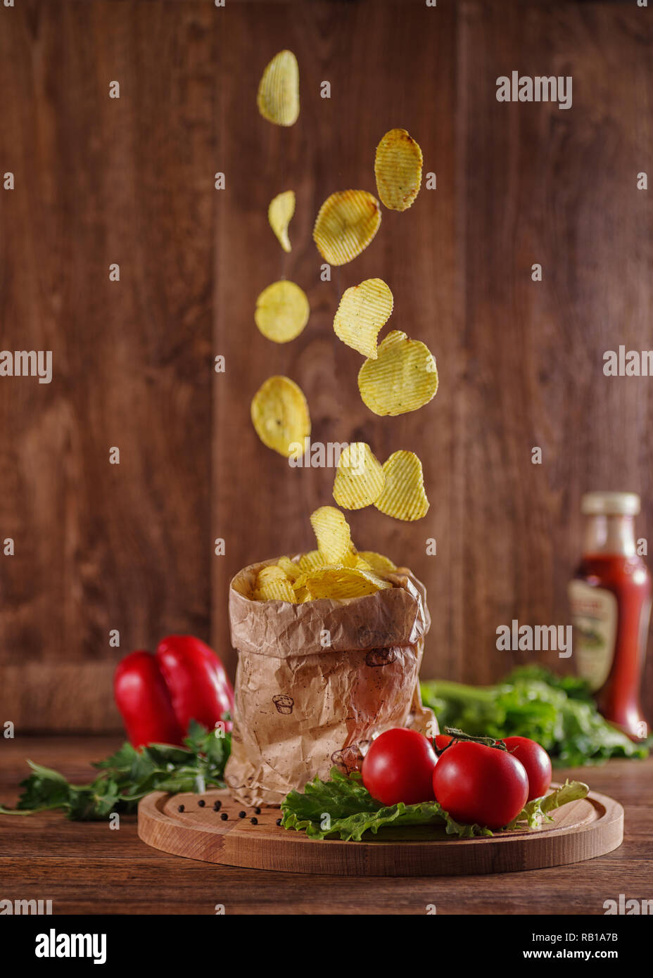Potato chips di cadere in un sacchetto di carta su un tavolo rustico. Foto Stock